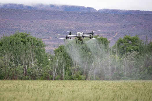 Aerial view of an agricultural drone spraying crops in a lush green field with mountains in the background.